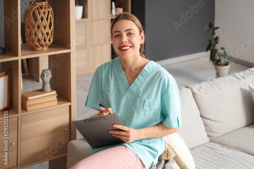 Young female medical student writing on clipboard and sitting on sofa at home