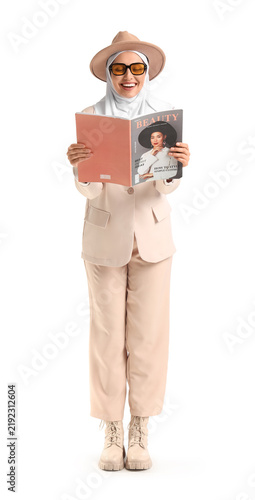 Stylish Muslim businesswoman in suit reading magazine on white background