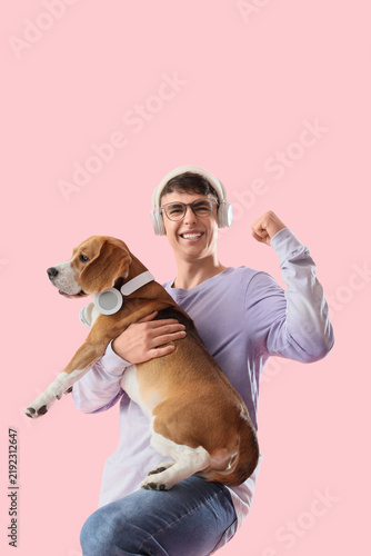 Young man in eyeglasses and headphones holding adorable Beagle dog on pink ba...