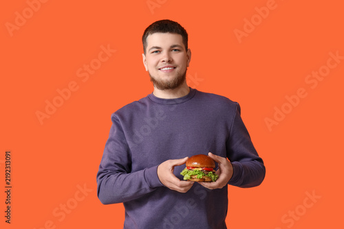 Young man with tasty burger on orange background