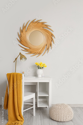 Vase with narcissus flowers, lamp and laptop on table in stylish room