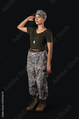 Confident young woman in military uniform saluting on black background