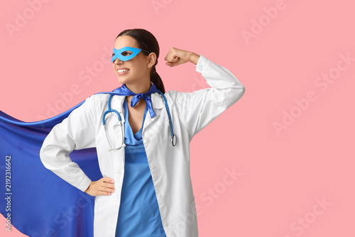 Beautiful female doctor in superhero costume showing muscles on pink background