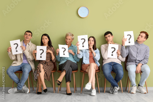 Applicants holding paper sheets with question marks near green wall in room