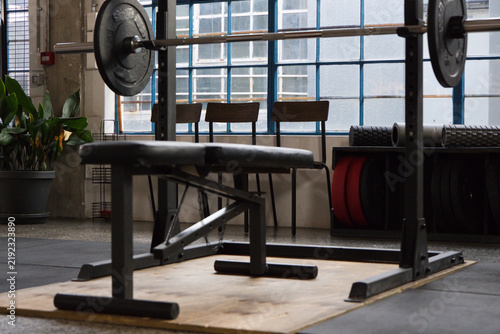 Adjustable bench sitting centered on wooden lifting platform with racked barbell and red plates