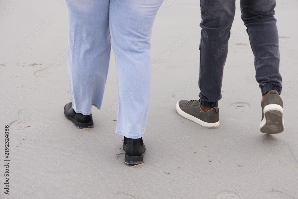 Obraz premium Couple walking on sand leaving footprints, wearing light blue pants and black boots, gray sneakers