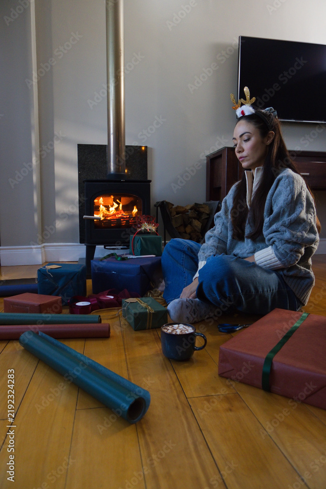 Obraz premium Lady sitting at home wearing sweater and festive headband wrapping gifts, mug near stove