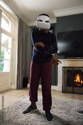 Foto African male youth wearing white virtual reality headset, standing on rug in liv