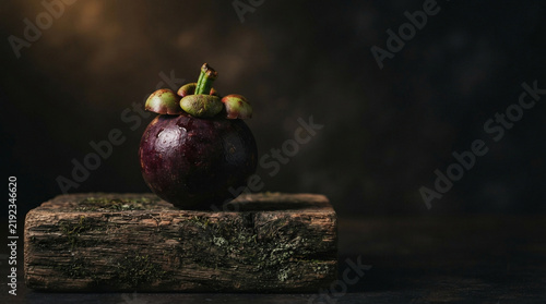 Side profile of a whole mangosteen with green calyx on aged cedar wood block