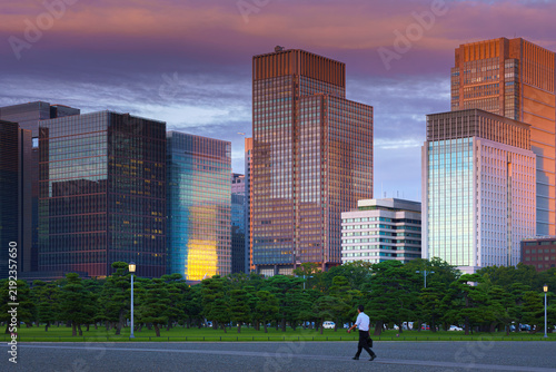 Tokyo, Japan - Oct 1 2024, panoramic view of the Chiyoda district's skyscrapers, with a parking lot with people walking in the foreground, and colorful clouds at sunset.Tokyo, Japan