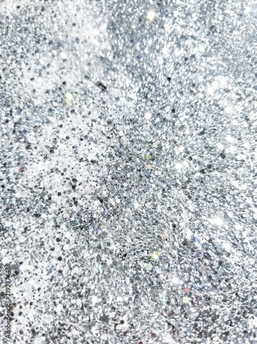 A close-up shot of a shimmering, silver glitter surface. The glitter particles reflect light, creating a dazzling, sparkling effect.
