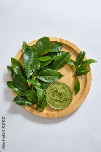 Green tea leaves and powdered tea arranged on a wooden tray, presenting two forms of the ingredient for tea packaging and natural product concepts.