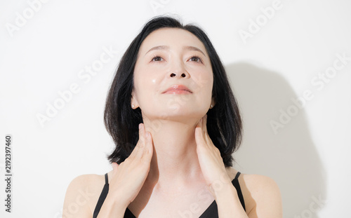 фотографія A woman in her 50s using both hands to care for her neck and décolletage; a beau