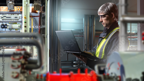Obraz na płótnie Industrial electrical maintenance, engineer uses a laptop to inspect and configure electrical control equipment and automation systems at a production facility