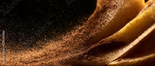 Cinnamon dust falls over sliced fruit in warm light, creating rich abstract food texture with flowing spice particles and dramatic contrast on dark background