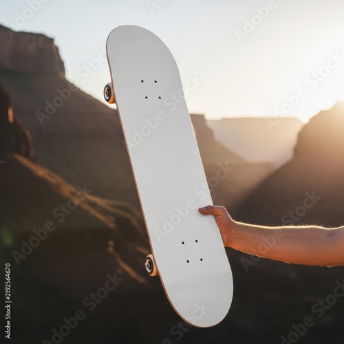 Person holding a blank skateboard deck outdoors at sunset