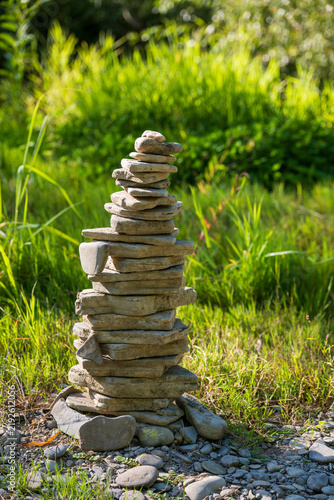 Canvas Print Stacked river stones forming a tall cairn on a sunny pebble riverbank, symbolizing balance, stability, harmony, mindfulness and connection with nature