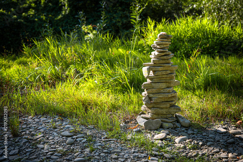 Photography Stacked river stones forming a tall cairn on a sunny pebble riverbank, symbolizing balance, stability, harmony, mindfulness and connection with nature