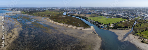 Aerial panorama of Kororoit Creek mouth entering Port Phillip Bay with tidal mudflats, saltmarshes, and industrial background in Altona and Williamstown, Melbourne, Victoria, Australia