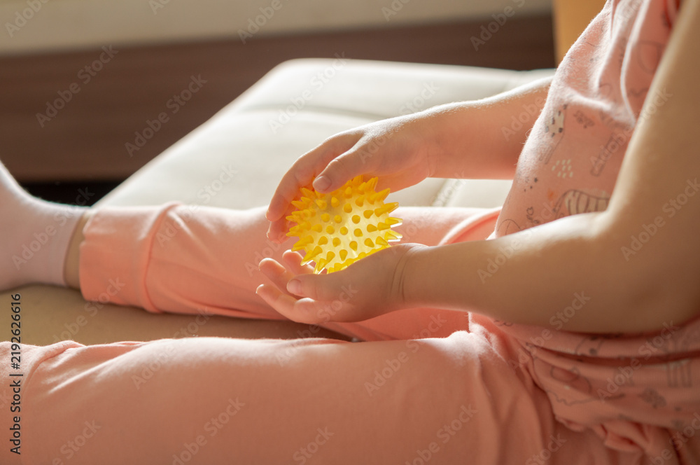 Obraz premium Macro of a child's hands squeezing and roll a yellow spiky massage ball. Concept of sensory therapy, pediatric acupressure, tactile learning, preschool fine motor skills development.