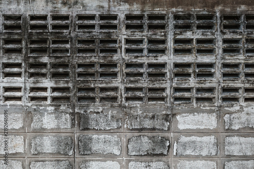 A photograph of an aged, weathered concrete and cinder block wall facade with a textured surface and rectangular ventilation blocks under daylight.
