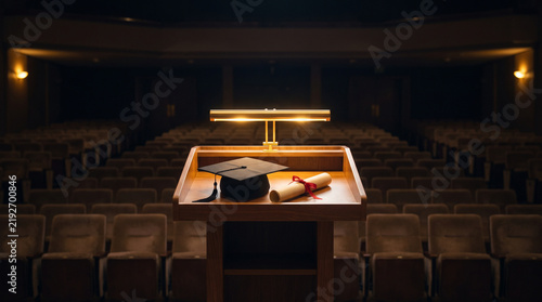 A graduation cap and diploma are placed on a podium in an empty auditorium.