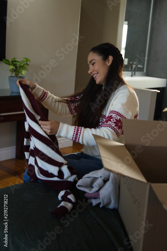 Принти на полотні Woman sitting on bed unpacking maroon-and-white sweater from box wearing white s