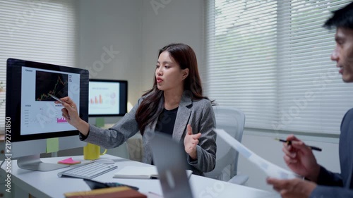 Businesswoman pointing at a computer screen showing financial charts and stock market data, discussing strategy with a male coworker