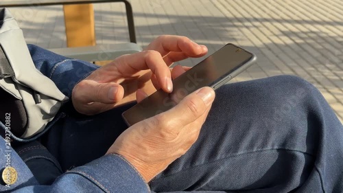 Browsing fast digital media content on smartphone touch screen outdoors. Mature person uses mobile internet app to scroll social network feed on bench. Doomscrolling concept explores