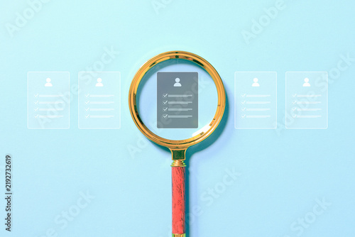 Magnifying glass highlights a candidate profile among applications, representing recruitment, resume screening, talent search, employee selection, hiring, and human resources. process.