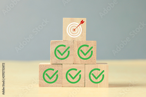 Wooden blocks with green check marks and a target with arrow symbolize goal achievement, successful planning, quality assurance, completed tasks, business strategy, and performance.