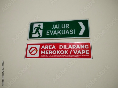 Fotografie Emergency exit evacuation route directional sign and no smoking or vaping warning sign mounted on a semi-outdoor balcony wall