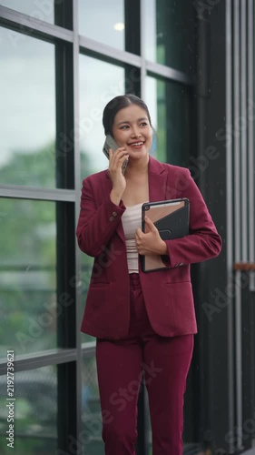 Successful asian businesswoman talking on the phone while walking outdoors in a modern city street with a tablet