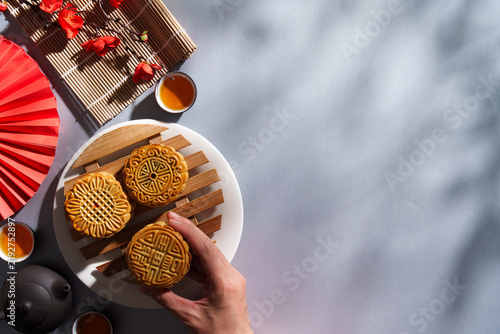Cropped hand holding mooncake with teapot and cups for Mid-Autumn Festival