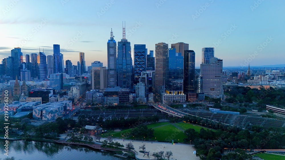 Fototapeta premium Melbourne, Victoria, Australia by night– 4K aerial drone view of Melbourne CBD skyline, Yarra River, Arts Centre, Flinders Street Station and illuminated skyscrapers at sunset twilight
