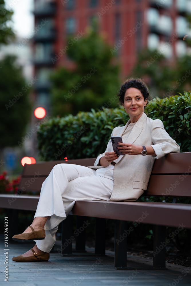 Obraz premium Woman using smartphone relaxing on park bench