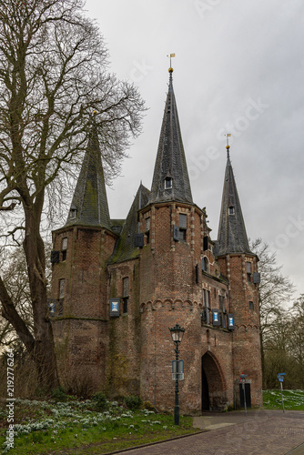 View of the historic Koornmarktspoort gatehouse with its distinctive brick towers and pointed roofs, set against a cloudy sky in Kampen, Overijssel, Netherlands.