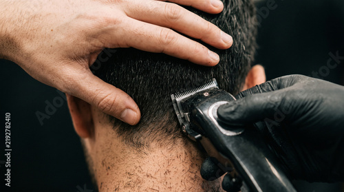 Extreme close-up of professional barber hands styling man hair with electric trimmer in modern barbershop, high detailed concept of male grooming, haircut, and personal care in minimalist aesthetic