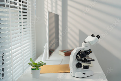 Modern science laboratory workspace with computer monitor and white microscope on white desk.
