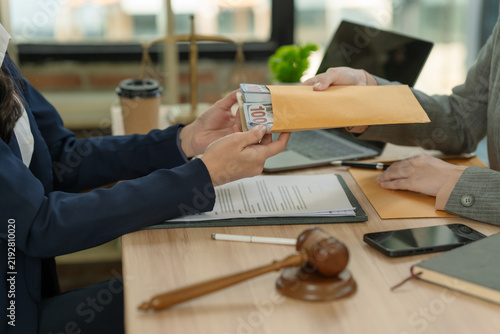 Quadro su tela Businessman giving bribe money in envelope to judge or lawyer at desk with wooden gavel and legal documents
