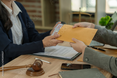Photography Businessman giving bribe money in envelope to judge or lawyer at desk with wooden gavel and legal documents