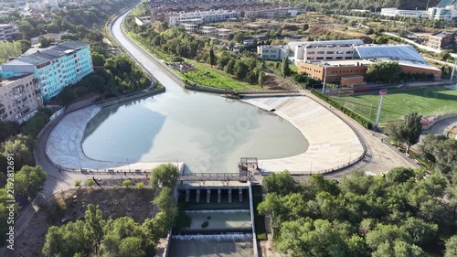 Aerial flyover above river park promenade toward mountains with luxury residential complexes at sunrise