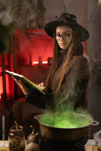 Foto A woman is holding a book of spells and looking into a cauldron