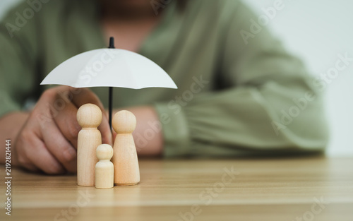 Fotografie Family insurance and protection with wooden figures under small umbrella