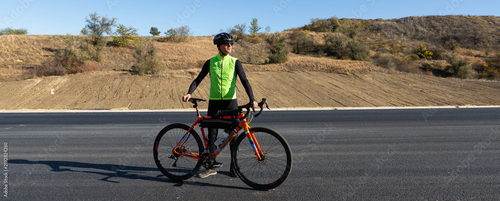 Obraz premium Cyclist riding bicycle on road against clear sky. A man in an outfit stands with a bicycle on an autumn sunny day.