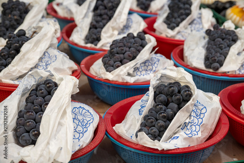Foto Clusters of fresh purple grapes wrapped in white paper bags rest inside colorful plastic baskets at a Korean market