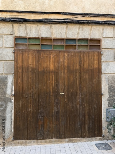 Weathered wooden garage door with colorful glass block transom window and exposed electrical wiring on a building facade in manacor, balearic islands, spain