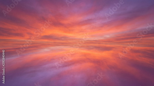 Crimson and Violet Sky Reflection: A breathtaking expanse of clouds ablaze with fiery orange and deep violet hues mirrors perfectly on a still body of water, creating a surreal, infinite horizon.