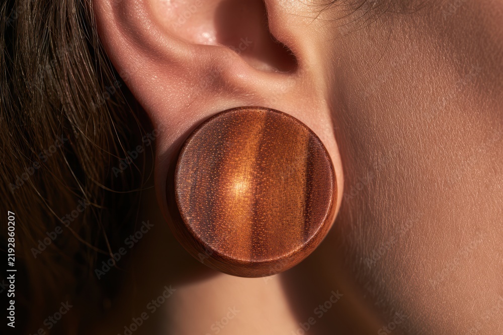 Fototapeta premium Person's earlobe showing a wooden plug earring as body modification jewelry