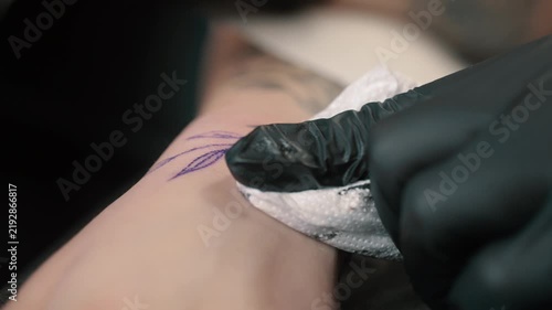 Professional tattoo artist creating a tattoo on a woman's forearm using a tattoo machine in a modern studio. Close up shot.